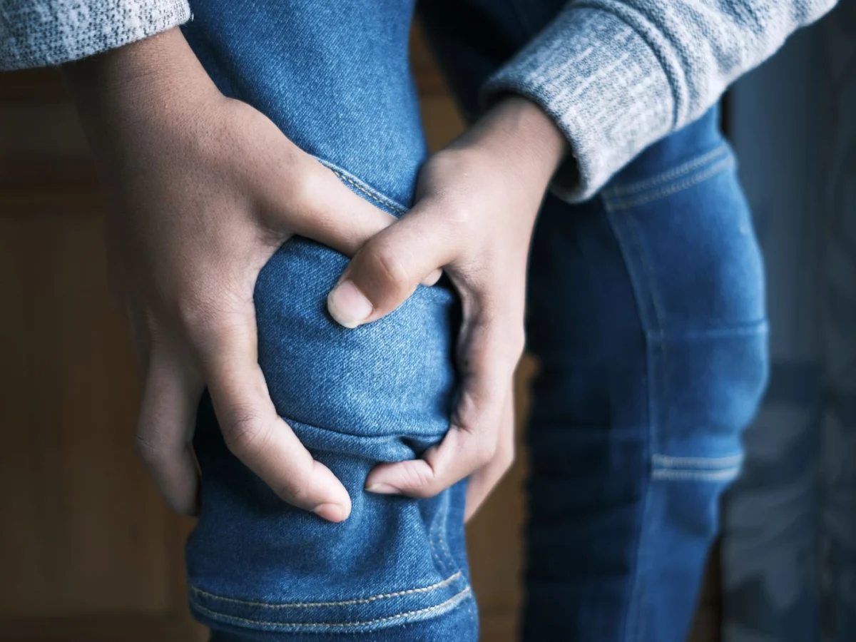 Χέρια σφίγγουν το γόνατο πάνω από το τζιν λόγω πόνου από ρήξη μηνίσκου